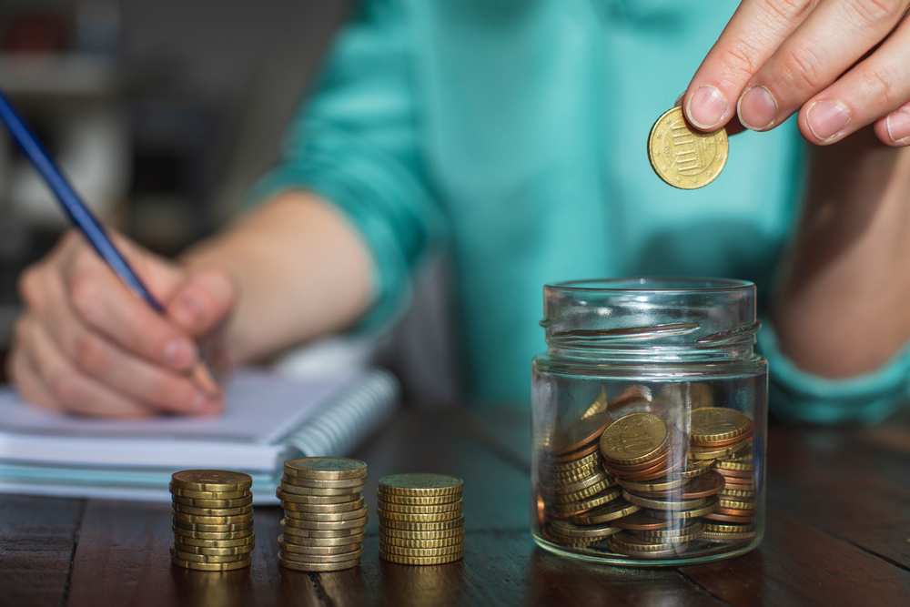 Persona ahorrando dinero en un frasco mientras registra sus finanzas personales. 

