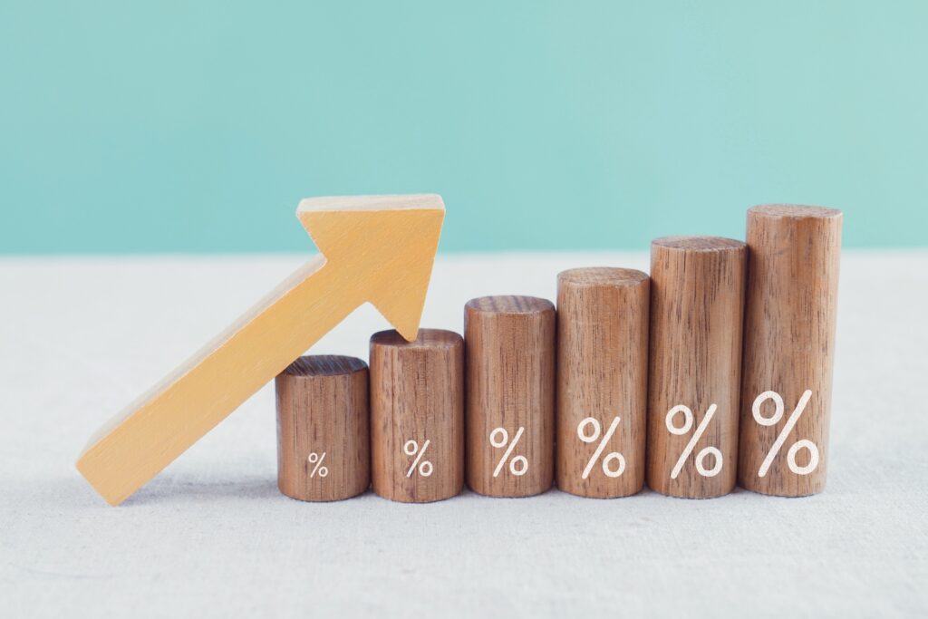 Gráfica ascendente formada por columnas de madera con símbolos de porcentaje, que representa el comportamiento de la tasa de interés, los intereses y su impacto en el costo del crédito.