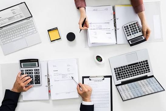 Vista superior de una mesa de trabajo con calculadoras, facturas, contratos y computadoras, que representa la gestión de cuentas por cobrar y el factoraje financiero. 
