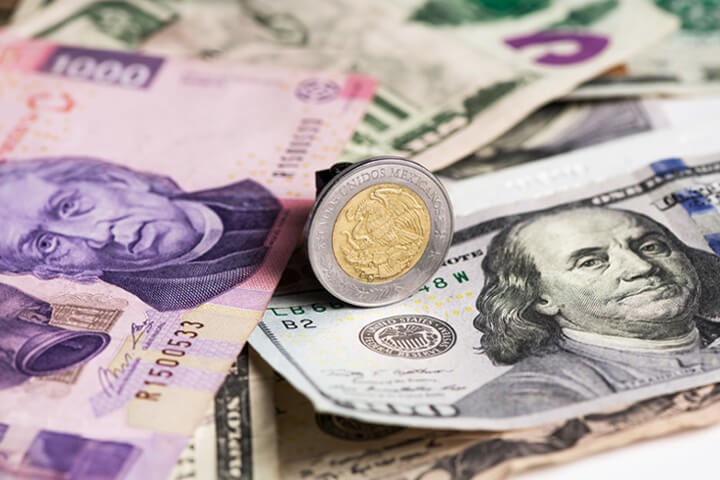 Moneda mexicana sobre billetes de pesos y dólares estadounidenses, representando la relación entre el peso mexicano y el dólar. 